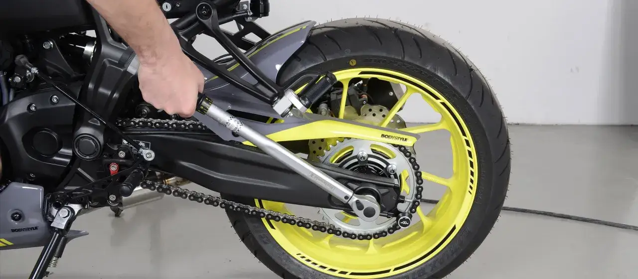 Ręka dokręca jarzmo zacisku kluczem dynamometrycznym, precyzyjnie regulując napięcie łańcucha motocykla.