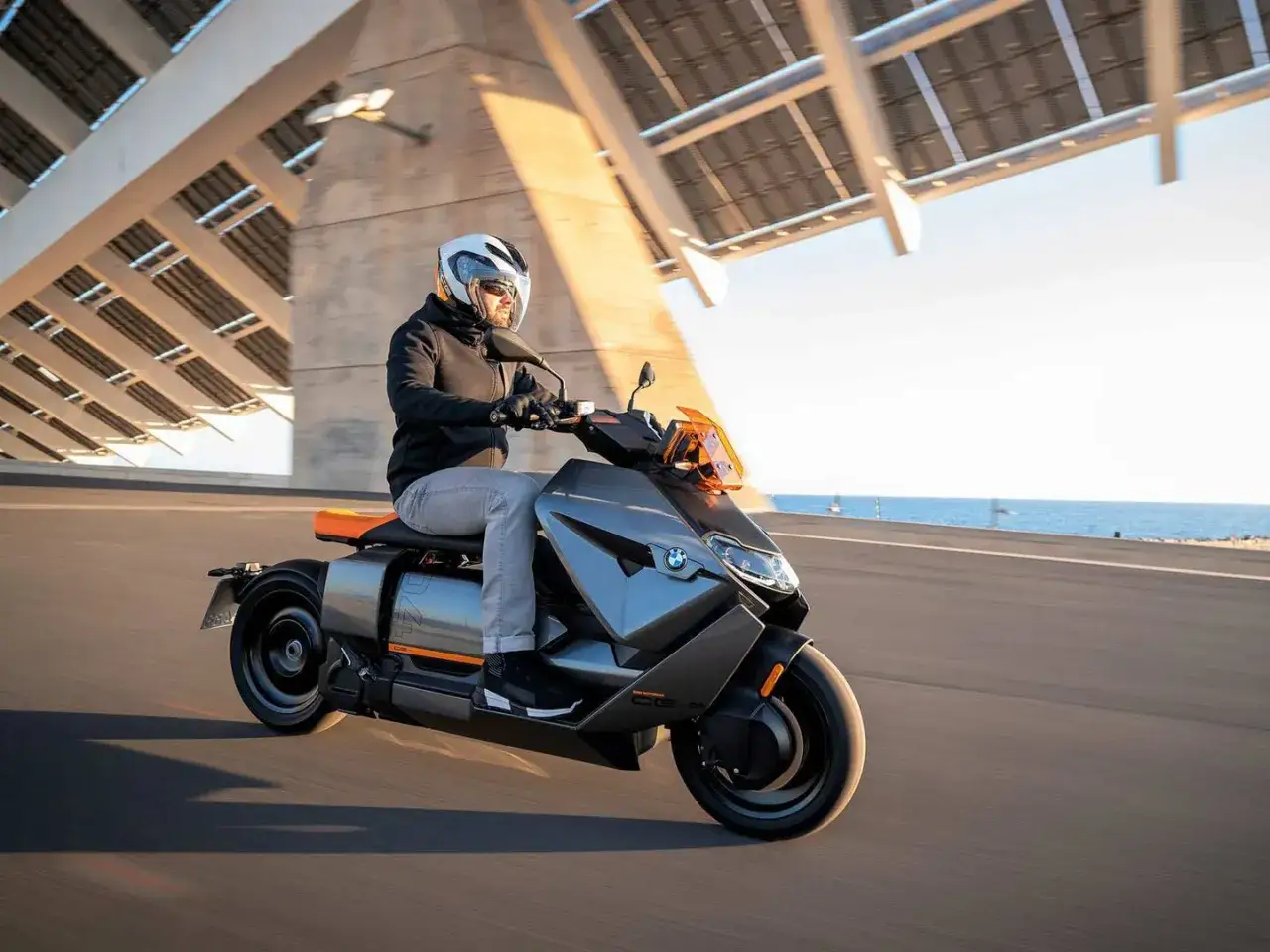 Mężczyzna w kasku jedzie na futurystycznym skuterze BMW CE04 wzdłuż wybrzeża.