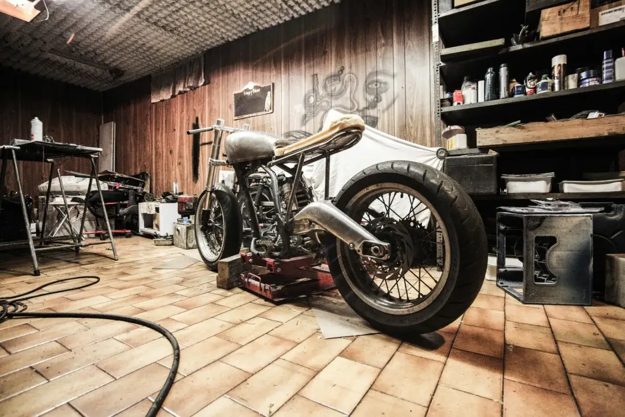 Motocykl w warsztacie, z widocznym zawieszeniem upside down. W tle regały z narzędziami i ścienna grafika.