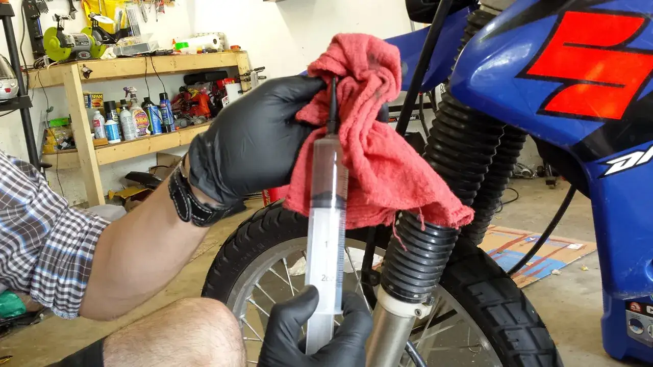 Rękawiczki i strzykawka pomagają w odpowietrzaniu hamulc&oacute;w motocykla.