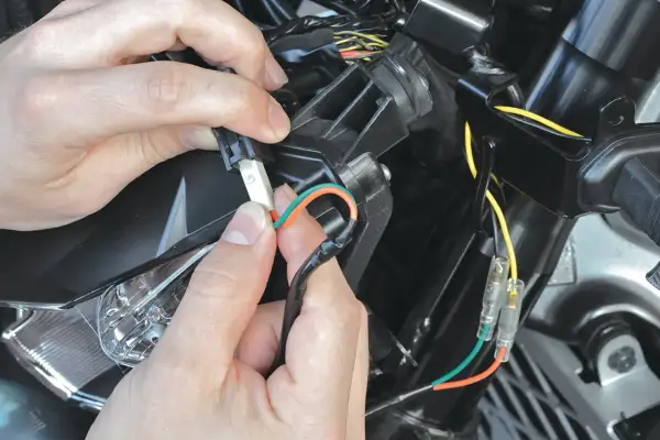 Ręce łączą przewody, pokazując, jak podłączyć kierunkowskazy LED w motocyklu. Pomarańczowy i zielony kabel są przygotowywane do połączenia.