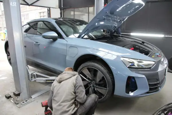 Mechanik pracuje przy niebieskim Audi na podnośniku. Zastanawiasz się, ile trwa wymiana opon z wyważeniem?