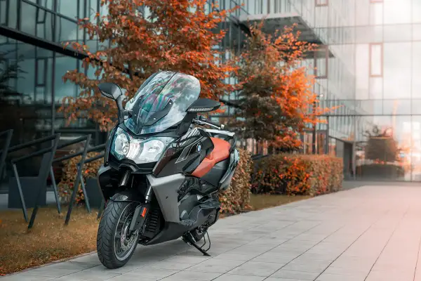 Elegancki skuter BMW C 650 GT z brązową kanapą stoi przed nowoczesnym budynkiem, otoczony jesiennymi drzewami.