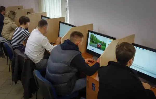 Ludzie siedzą przy komputerach, rozwiązując testy. Zastanawiają się, ile trzeba mieć punktów, żeby zdać egzamin teoretyczny.
