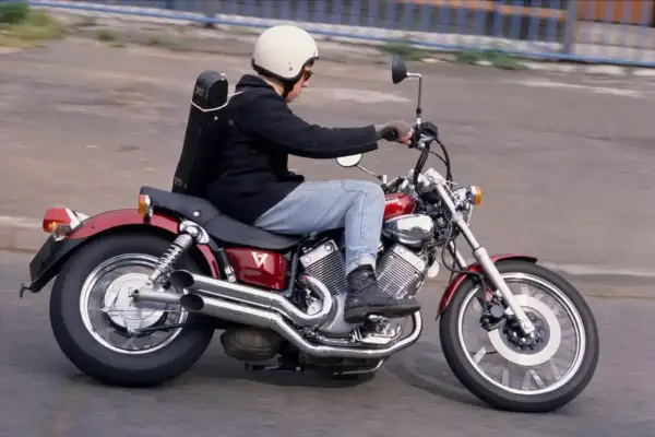 Mężczyzna w kasku jedzie na czerwonym motocyklu Yamaha Virago, z futerałem na instrumenty muzyczne na plecach.