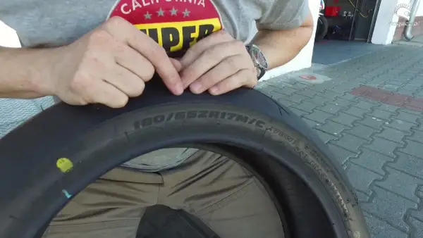 Ręce wskazują na oznaczenia na oponie motocyklowej, pomagając zrozumieć, jak dobrać opony. Widoczny rozmiar 180/55ZR17.