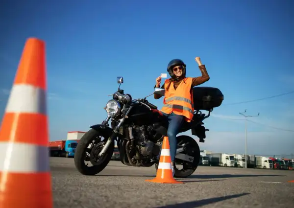 Szczęśliwa motocyklistka z radością prezentuje swoje nowe prawo jazdy kat A, siedząc na motorze na placu manewrowym.