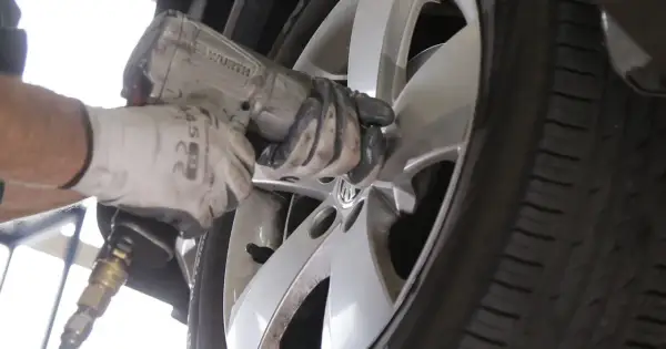 Mechanik w białej rękawicy dokręca śruby w feldze, zastanawiając się, ile km wytrzymują opony.