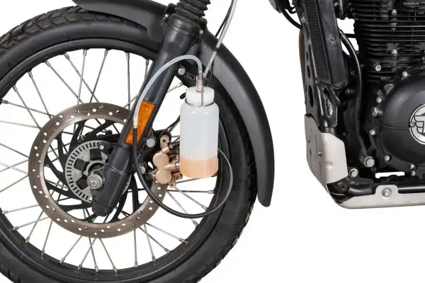 Zbiorniczek z płynem do odpowietrzania hamulców motocykla, podłączony do zacisku hamulcowego przy przednim kole.