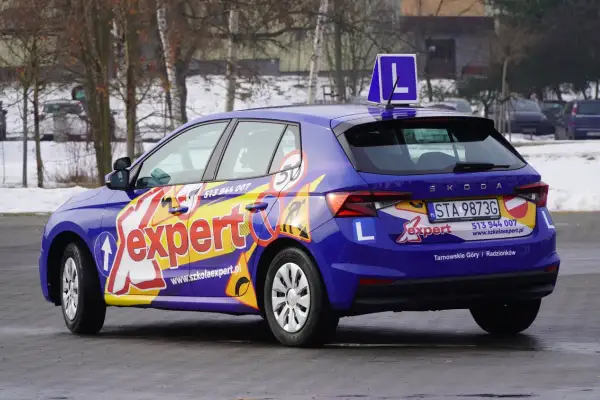 Niebieski samochód szkoleniowy z napisem "expert" i literą "L" na dachu. Zapytaj, ile trwa kurs na prawo jazdy kat A.