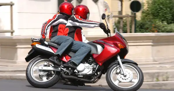 Dwie osoby w czerwonych kaskach i kurtkach jadą na czerwonym motocyklu. To ich pierwsza jazda 125 na dwóch, bez 3 lat doświadczenia.