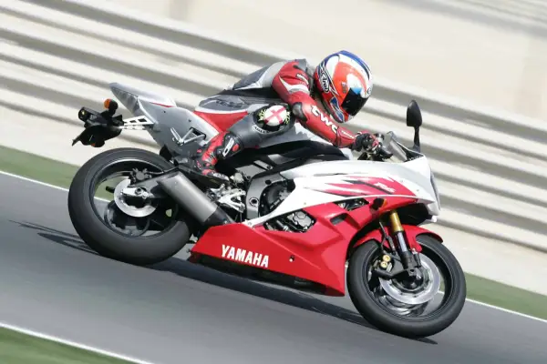 Motocyklista w czerwonym kombinezonie śmiga na torze Yamahą R6. Od ilu lat można robić prawo jazdy na motor 600? Od 20 lat na kategorię A.